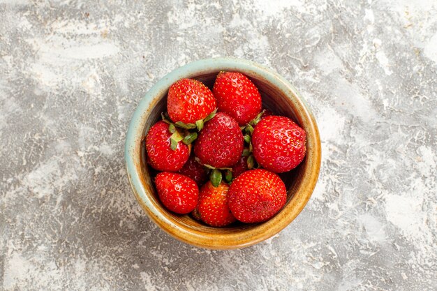 Vista superior de fresas rojas frescas dentro de una pequeña olla en la superficie blanca de frutos rojos de frutas