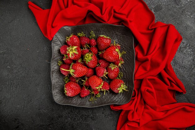 Vista superior de fresas rojas frescas dentro de la placa en la baya de la fruta del piso oscuro