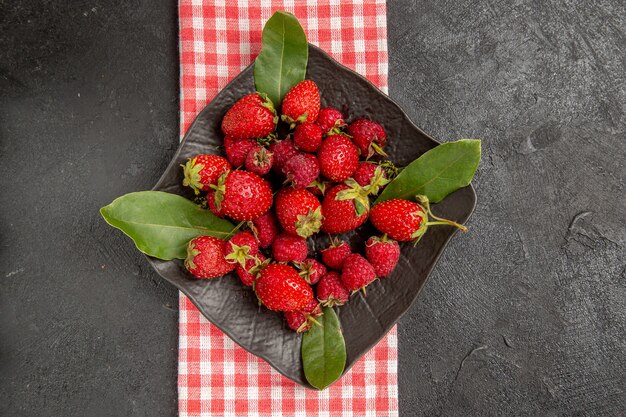 Vista superior de fresas rojas frescas dentro de la placa en la mesa oscura color baya frambuesa