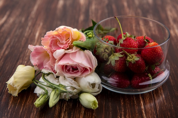 Foto gratuita vista superior de fresas rojas frescas en un recipiente con hermosas flores como tulipán y rosas sobre un fondo de madera