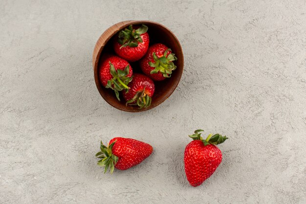 Vista superior fresas rojas frescas suaves jugosas dentro de una olla marrón en el piso gris