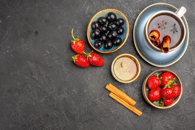 Vista superior de fresas rojas frescas con té y aceitunas en fruta fresca de baya de superficie oscura