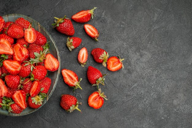 Vista superior de fresas rojas en rodajas y frutas enteras sobre fondo gris