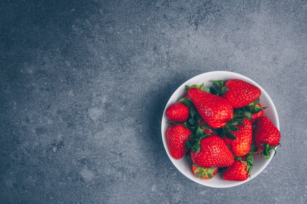 Vista superior de fresas en un tazón sobre fondo gris con textura. espacio horizontal para texto