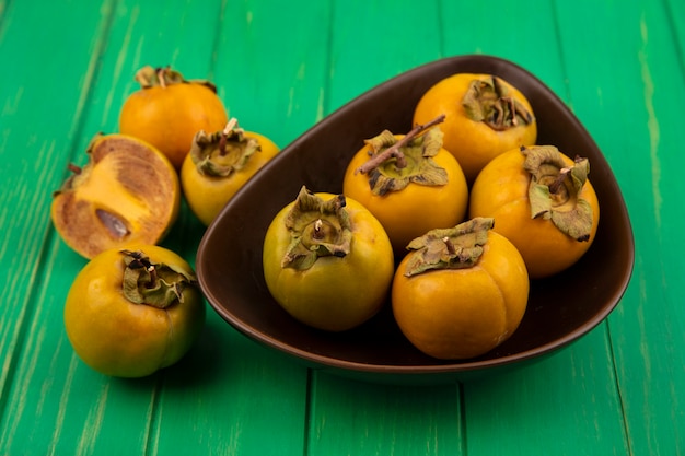 Vista superior de frutas de caqui frescas y saludables en un recipiente sobre una mesa de madera verde