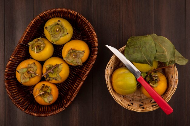 Vista superior de frutas de caqui orgánico en un balde con cuchillo sobre una mesa de madera