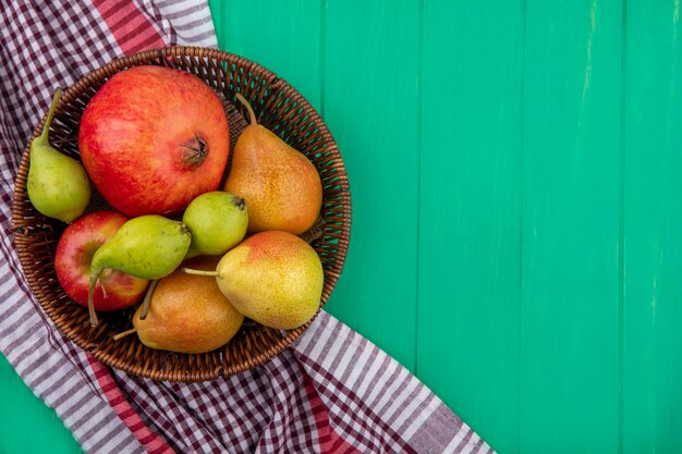 Vista superior de frutas en la cesta sobre tela escocesa sobre superficie verde