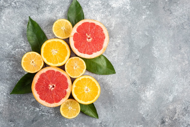 Vista superior de frutas cítricas frescas, frutas medio cortadas en mesa gris.