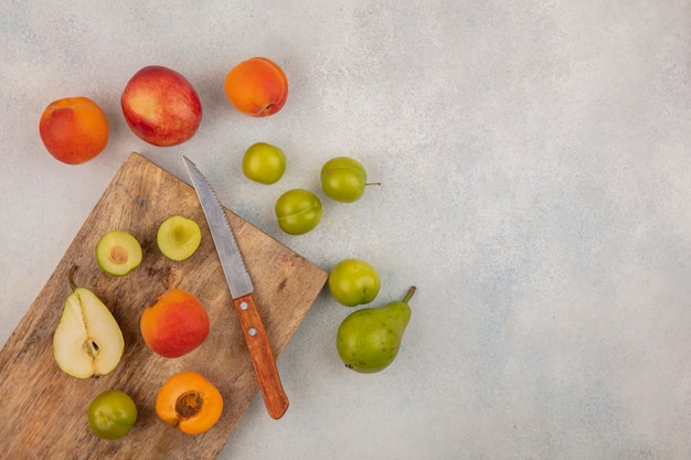 Vista superior de frutas como albaricoque de ciruela pera medio cortado con cuchillo en la tabla de cortar y patrón de melocotón de albaricoque de ciruela pera sobre fondo blanco con espacio de copia