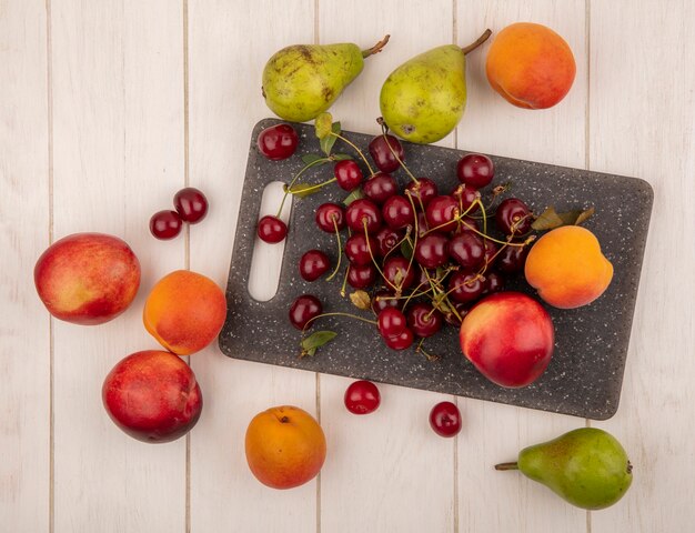 Vista superior de frutas como cerezas y melocotones en tabla de cortar y patrón de peras cerezas y melocotones sobre fondo de madera