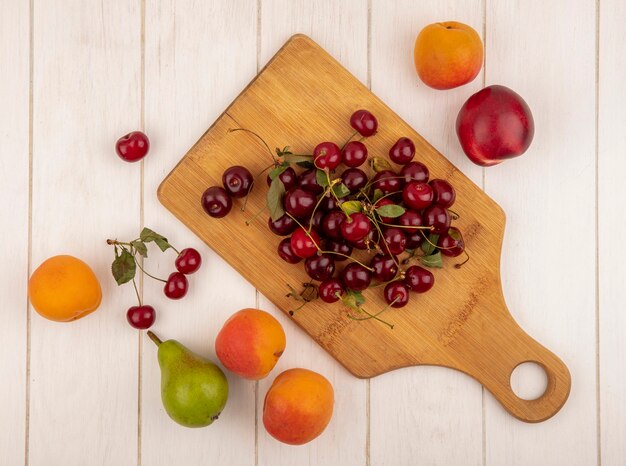 Vista superior de frutas como cerezas en tabla de cortar con melocotones y peras sobre fondo de madera