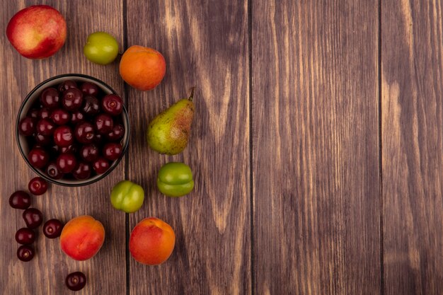 Vista superior de frutas como cerezas en un tazón y patrón de melocotón ciruelas albaricoques cerezas de pera sobre fondo de madera con espacio de copia