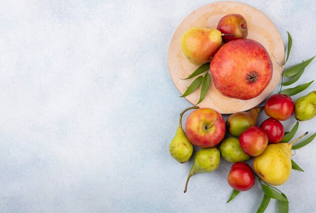 Vista superior de frutas como ciruela durazno y granada en tabla de cortar y con manzana en superficie blanca con espacio de copia