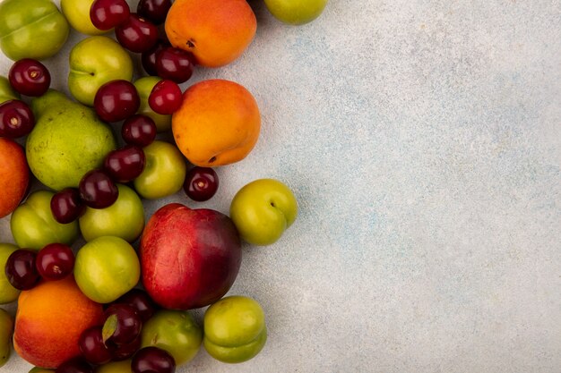 Vista superior de frutas como ciruela melocotón albaricoque cereza y pera sobre fondo blanco con espacio de copia