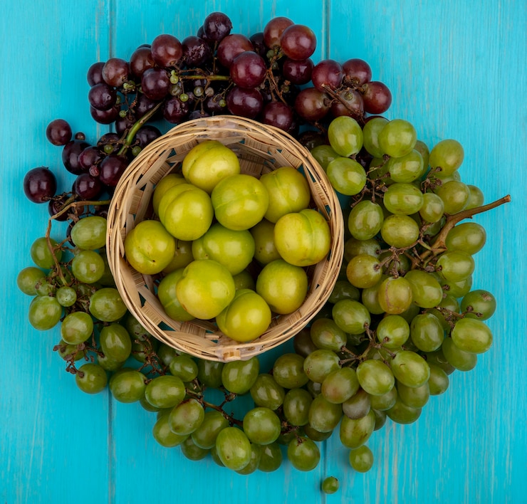 Foto gratuito vista superior de frutas como ciruelas en canasta y uvas alrededor sobre fondo azul.