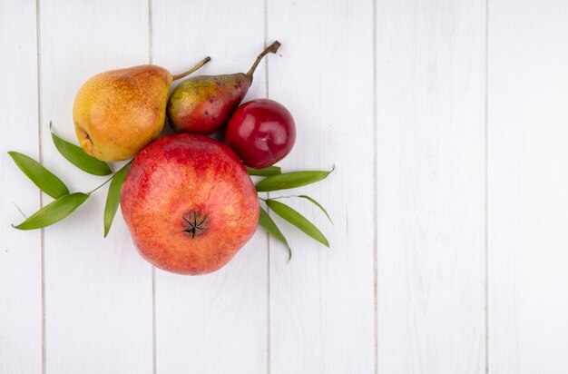 Vista superior de frutas como durazno granada de ciruela con hojas en la superficie de madera con espacio de copia