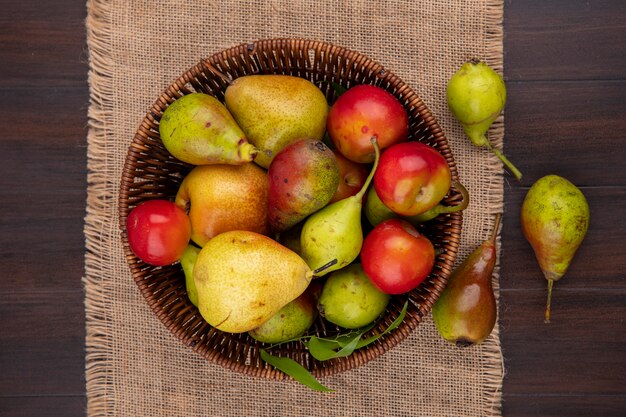 Vista superior de frutas como durazno manzana ciruela en canasta y tela de saco sobre superficie de madera