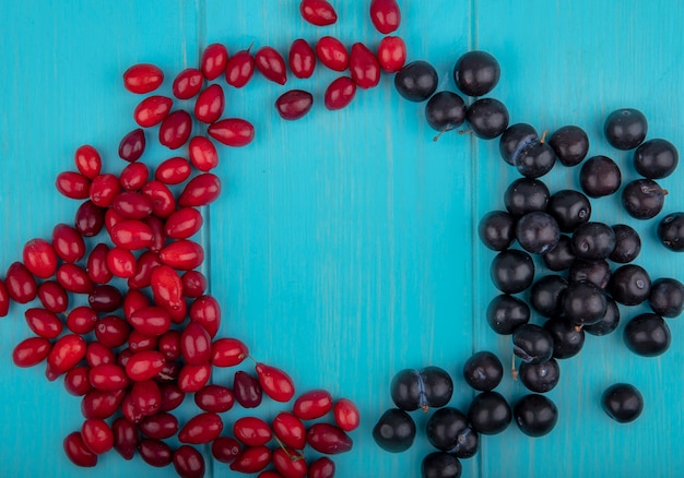 Vista superior de frutas como endrinas y bayas de cornel en forma redonda sobre fondo azul con espacio de copia