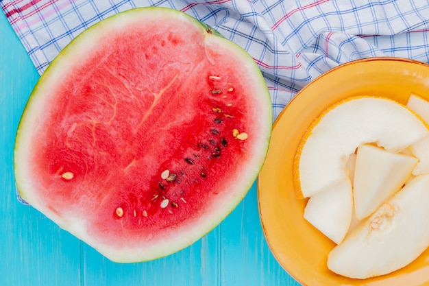 Vista superior de frutas como la mitad de sandía y el plato de rodajas de melón sobre tela escocesa y fondo azul.