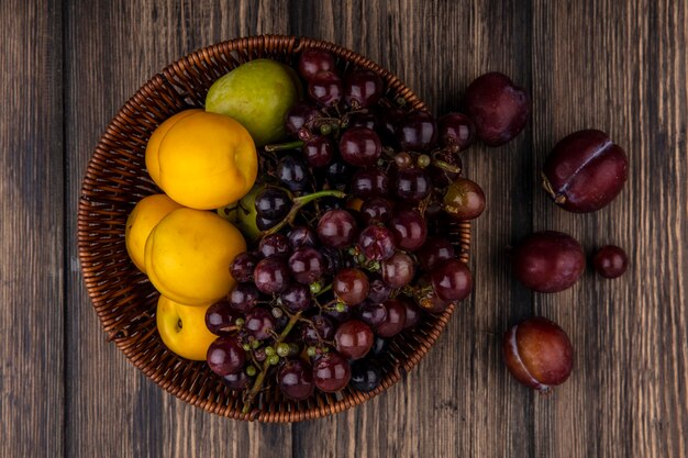 Vista superior de frutas como nectacots pluot de uva en canasta y pluots rey de sabor sobre fondo de madera