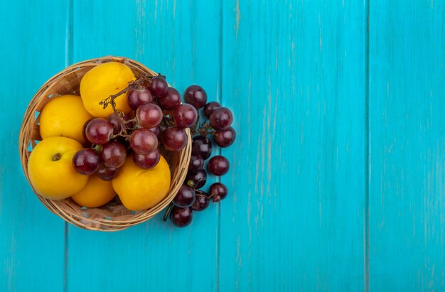 Vista superior de frutas como nectacots y uva en canasta y sobre fondo azul con espacio de copia