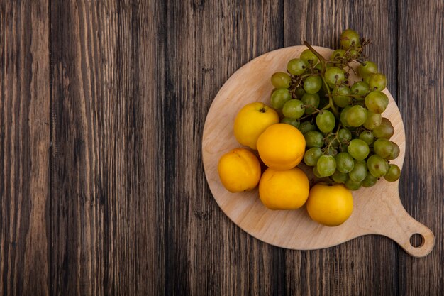 Vista superior de frutas como nectacots y uva en tabla de cortar sobre fondo de madera con espacio de copia