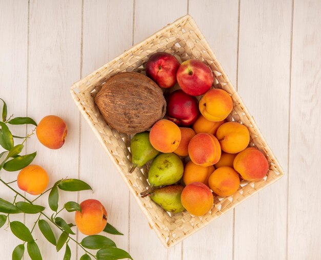 Vista superior de frutas como pera de durazno de coco en canasta con hojas sobre fondo de madera