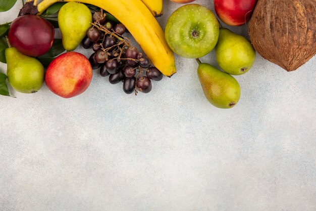 Vista superior de frutas como pera manzana uva melocotón coco plátano sobre fondo blanco con espacio de copia