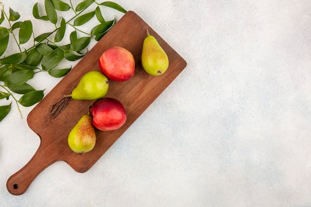 Vista superior de frutas como peras y melocotones en tabla de cortar con hojas sobre fondo blanco con espacio de copia