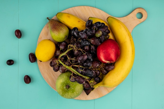 Foto gratuita vista superior de frutas como plátano manzana limón uva melocotón pera en tabla de cortar sobre fondo azul.
