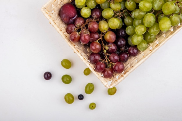 Foto gratuita vista superior de frutas como pluot y uvas en canasta y bayas de uva sobre fondo blanco.