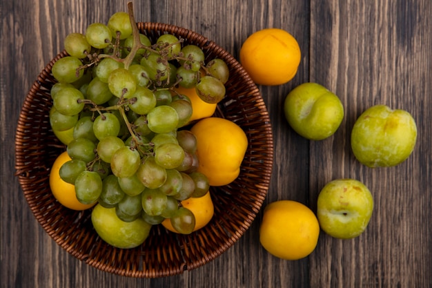 Vista superior de frutas como pluot verde uva y nectacots en canasta y patrón de pluots y nectacots sobre fondo de madera