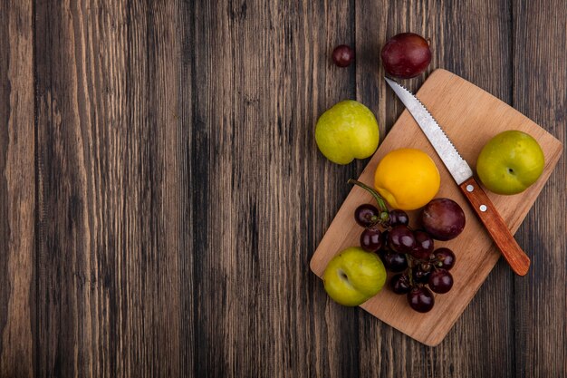 Vista superior de frutas como pluots de nectacot de uva con cuchillo sobre tabla de cortar sobre fondo de madera con espacio de copia