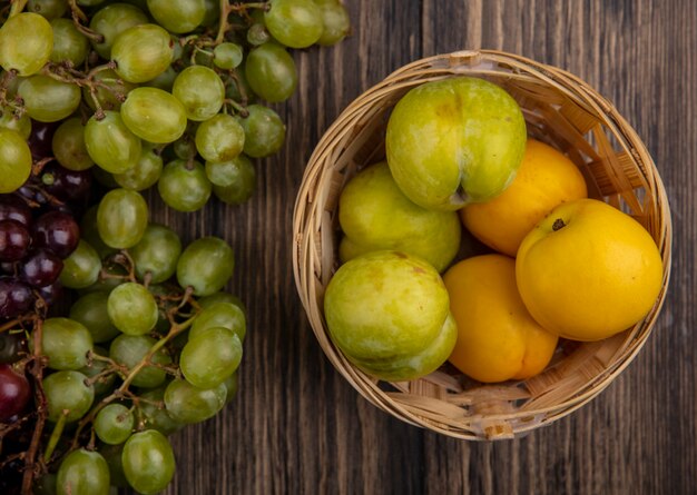 Vista superior de frutas como pluots y nectacots en canasta y uvas sobre fondo de madera