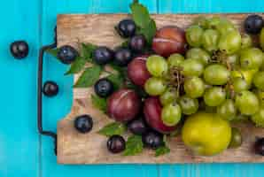 Foto gratuita vista superior de frutas como pluots de uva con bayas de uva y hojas sobre tabla de cortar sobre fondo azul.