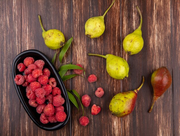 Vista superior de frutas como tazón de frambuesa y duraznos con hojas sobre superficie de madera