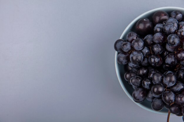 Vista superior de frutas como uva y endrinas en un recipiente sobre fondo gris con espacio de copia