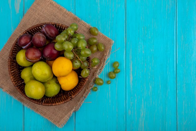 Vista superior de frutas como uva pluots nectacots en canasta y bayas de uva en tela escocesa y sobre fondo azul con espacio de copia