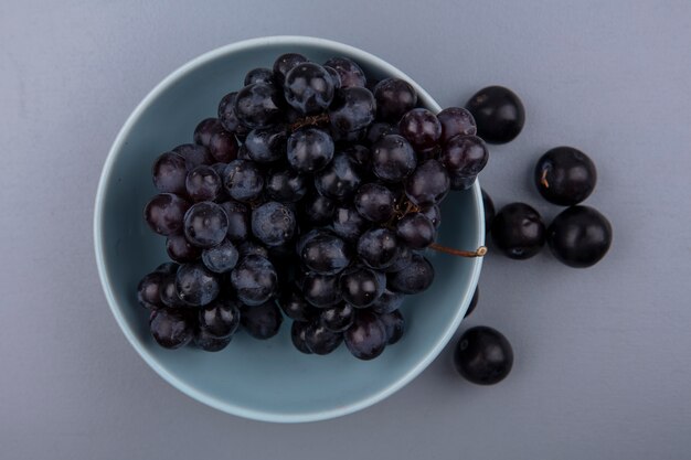 Vista superior de frutas como uva en un tazón y endrinas sobre fondo gris