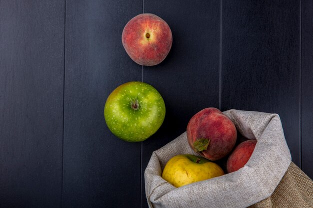 Vista superior de frutas frescas y coloridas como melocotones y manzanas en bolsas de arpillera en negro