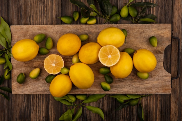 Vista superior de frutas frescas como kinkans y limones en una tabla de cocina de madera en una pared de madera