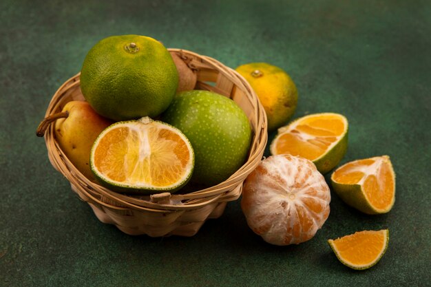 Vista superior de frutas frescas como mandarinas manzanas pera kiwi en un balde con mandarinas a la mitad aislado