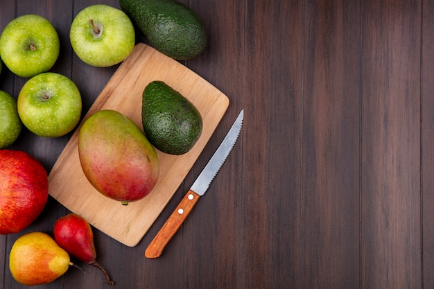 Vista superior de frutas frescas como mango y aguacate en tablero de cocina de madera con cuchillo y manzanas verdes en madera con espacio de copia