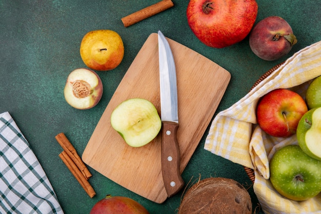 Vista superior de frutas frescas como manzana en tablero de cocina de madera con cuchillo durazno granada pera y ramas de canela en verde