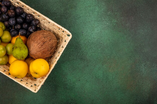 Vista superior de frutas frescas como pera verde melocotón amarillo coco en un cubo sobre un fondo verde con espacio de copia