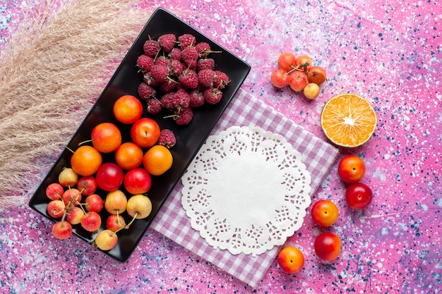 Foto gratuita vista superior de frutas frescas frambuesas y ciruelas dentro de forma negra sobre la superficie rosa