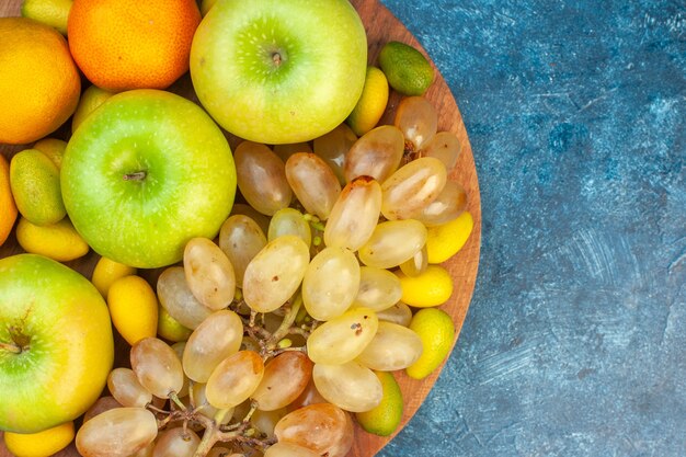 Vista superior de frutas frescas, manzanas, mandarinas y uvas en el jugo de mesa azul, fruta suave, color fotográfico, composición de vida saludable