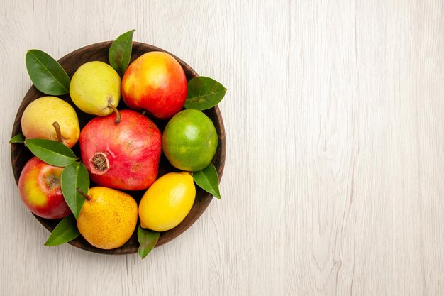 Vista superior de frutas frescas manzanas, peras y otras frutas dentro de la placa en el escritorio blanco frutas color de árbol maduro suave muchos frescos