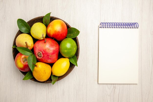 Vista superior de frutas frescas manzanas, peras y otras frutas dentro de la placa en el escritorio blanco frutas color de árbol maduro suave muchos frescos