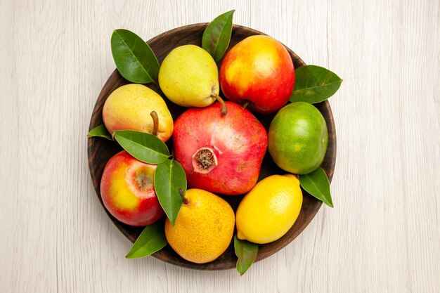 Vista superior de frutas frescas manzanas, peras y otras frutas dentro de la placa en el escritorio blanco frutas color de árbol maduro suave muchos frescos